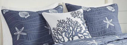Layered coastal bedroom with soft blue bedding, natural textures, and relaxed seaside styling
