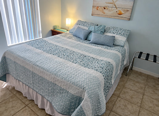 Soft coastal bedding in muted blue and white tones styled in a bright bedroom