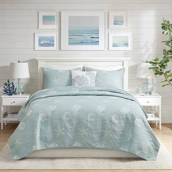 Aqua seashell and starfish quilt on a bed in a bright coastal bedroom