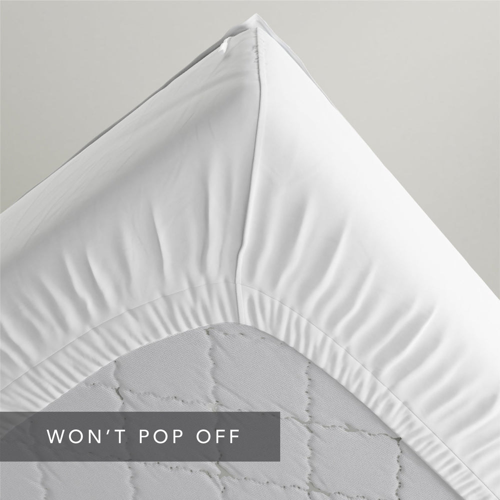 A close-up of a white  Quickzip Fitted Sheet corner pulled tightly over the corner of a light gray quilted mattress, with a dark gray banner at the bottom reading 'WON'T POP OFF'.