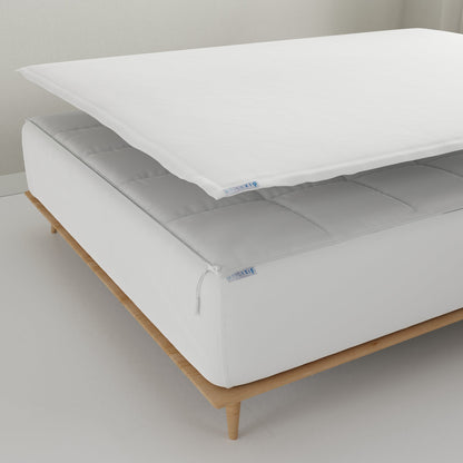 A white Quickzip Fitted Sheet is shown partially lifted over a white mattress on a light wood bed frame in a clean, minimalist room setting.
