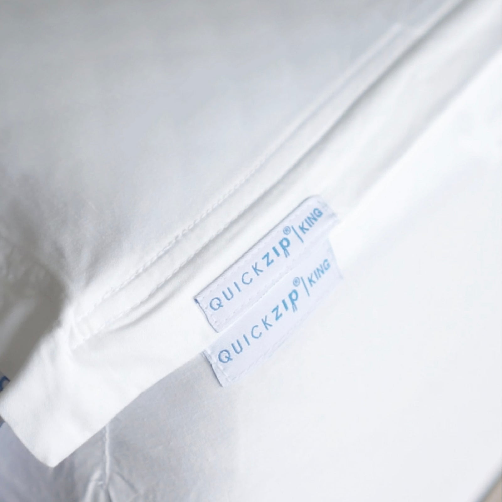 Close-up of a white bedding item, a  Quickzip Fitted Sheet , with two white labels reading QuickZip King.