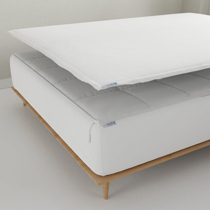 A white Quickzip Fitted Sheet is shown partially lifted over a white mattress on a light wood bed frame in a clean, minimalist room setting.